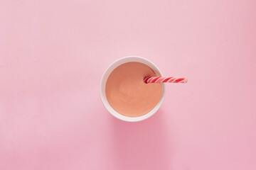  Top view of Candy cane on a white deep plate with pudding on a pink pastel background. Minimal holiday or food concept.