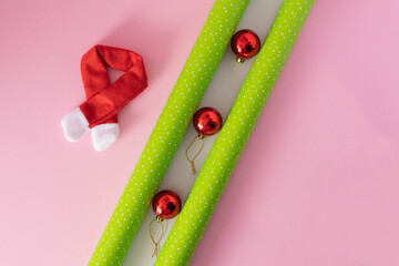 Christmas green wrapping paper, red ornaments, and a red and white scarf against a pink background....