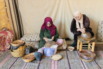 Muslim women sitting outdoors while crushing argan nuts on stone mill © julio