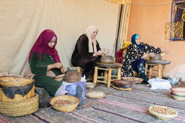 Muslim women sitting outdoors while crushing argan nuts on stone mill