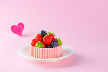 Tartlet or cake with strawberries, raspberries, blueberries and a basket of pink chocolate in a plate and heart on a pink background.