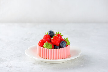 Tartlet or cake with strawberries, raspberries, blueberries and a basket of pink chocolate in a plate.