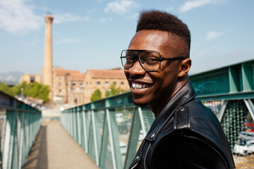 Portrait of smiling young stylish african american man wears eyeglasses and leather jacket,...