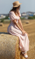 A girl in a dress and hat sits on a haystack