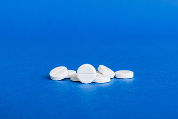 Heap of white pills on colored background. Tablets scattered on a table. Pile of red soft gelatin...
