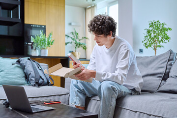 Young male unpacking an online purchase, with box with new smartphone