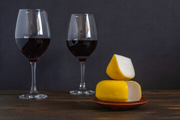 Gouda cheese on the background of red wine and dark wood.
