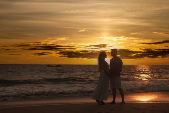 Silhouettes of couple in love kissing and embracing at tropical sea sunset, full body. Male and female togetherness posing on sandy beach outdoor. Summer vacation lifestyle concept. Copy ad text space