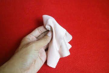 A hand holding a cloth that serves to wipe glasses, on a red background