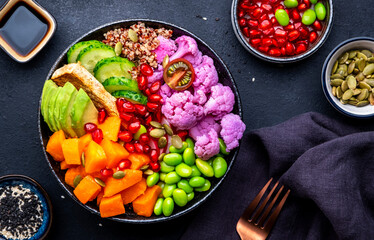 Vegan buddha bowl with baked pumpkin, quinoa, avocado, edamame soybeans, fried tofu, cauliflower, pomegranate and seeds, black table background, top view. Autumn or winter healthy vegetarian food