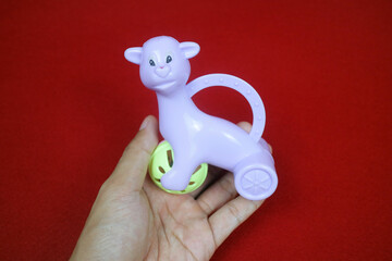 A hand holding A toy shaped like an alpaca animal, purple color, holding a ball. on a red background