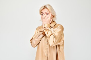 Portrait of young blonde woman covering eyes with hand, peeking through fingers isolated on white...