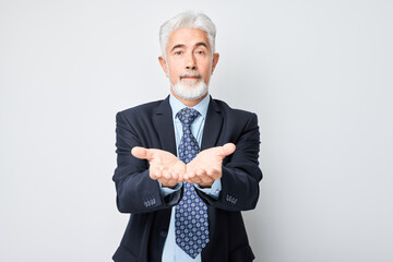 Gray-haired mature man 60 years old in business suit holding something in hand, demonstrating empty space for product or text isolated on white studio background.