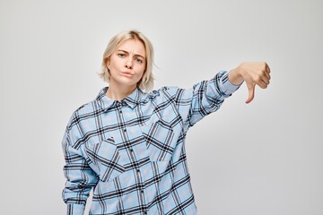 Portrait of blond girl in plaid shirt showing thumbs down isolated on white studio background....