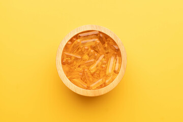 Oil softgel capsules in wooden bowl on yellow background. Nutritional supplement contains fish oil,...
