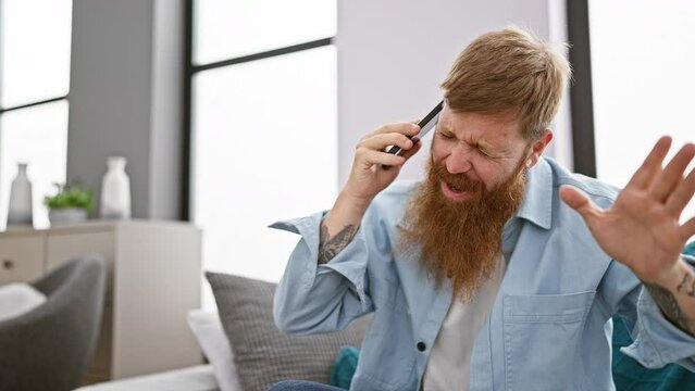 Irish redhead man, sitting in the living room, stressed about his conversation on his smartphone, fighting with frustration and despair