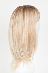 Naklejka premium Natural looking blonde fair wig on white mannequin head. Middle length hair cut on the plastic wig holder isolated on white background, side view.