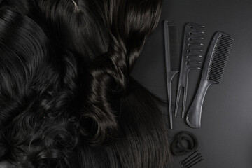 Hairdresser tools close-up isolated on black background. Curls of dark brunette hair and a set of...