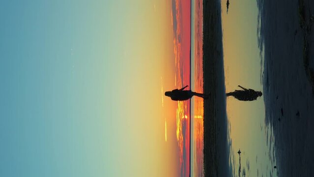 Romantic girl walks on the coast, pink and turquoise sunset and the sun setting over the horizon vertical