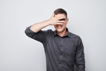 Portrait of young businessman covering eyes with hand, peeking through fingers isolated on white...