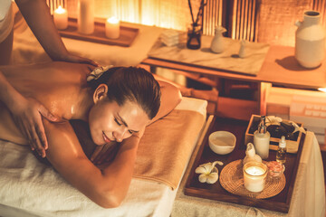 Caucasian woman customer enjoying relaxing anti-stress spa massage and pampering with beauty skin recreation leisure in warm candle lighting ambient salon spa at luxury resort or hotel. Quiescent - obrazy, fototapety, plakaty