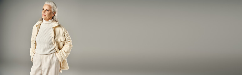 grey haired middle aged woman in trendy winter outfit posing with hands in pockets, banner