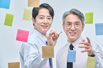 Two businessmen are standing on the glass wall of the office, looking at the attached paper and...