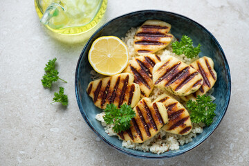 Blue bowl with grilled halloumi cheese and couscous, horizontal shot on a beige stone background, elevated view