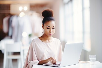 A modern black businesswoman with a laptop, working in a sleek clothes shop.