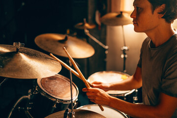 Drummer plays drums in music studio at band rehearsal. Musician with instrument in beautiful sunset...