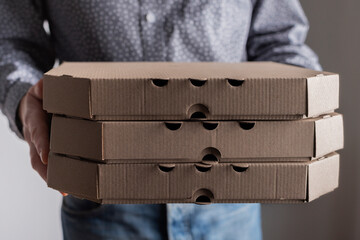 Caucasian male hands hold three pizza boxes front view with copy-space