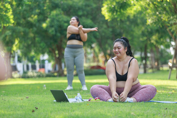 Fototapeta na wymiar Asian female overweight in sportswear training exercise to lose weight on mat looking preview with laptop. woman plus size training online practice yoga in park. concept of healthy.