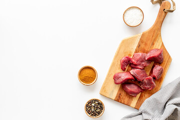 Raw beef meat cutting into pieces on wooden board with spices