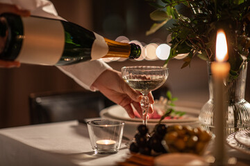 holidays, dinner party and celebration concept - close up of hand pouring champagne from bottle to...