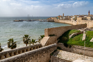 Fototapeta na wymiar A fortified sea wall, a small boat harbor, mosque minarets and church towers all constructed from stone blocks, the old city of Acre, Israel