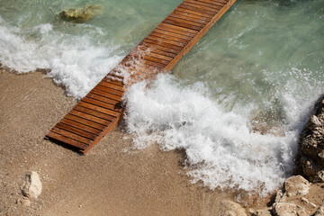 Aerial view of wooden pier with waves breaking on the shore, turquoise clear water