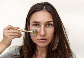millennial woman using derma roller for face rejuvenation. isolated girl on beige background,close...