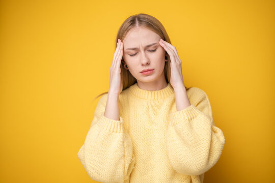 Portrait of a cute girl suffering from a headache on a yellow background. Young woman suffering from migraine.