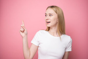 A cute girl stands on a pink background and points to a place for text. Banner or advertising...