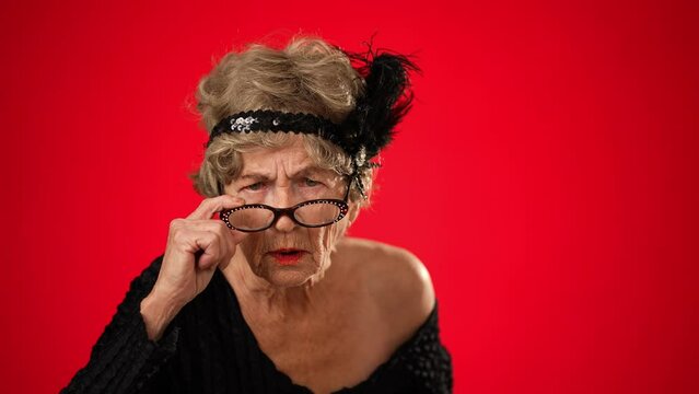 Funny view of unhappy displeased frustrated elderly woman saying NO wearing wig, glasses and no teeth isolated on red background