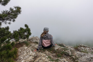 A picturesque mountain landscape in the clouds on Ai-Petri mountain in the Crimea. A woman on the background of a high-altitude landscape with trees in the clouds. Fog on the mountain.