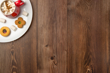 Plate with cookies and mug of hot chocolate with marshmallows on wooden background. Space for text.