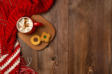 Mug of hot chocolate and cookies with soft red winter scarf on wooden background. Top view