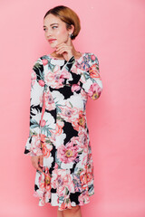 Portrait of beautiful slender fashionable young woman in dress with flowers on pink background