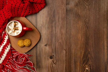 Mug of hot chocolate and cookies with soft red winter scarf on wooden background. Top view