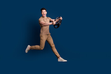 Fototapeta na wymiar Full size photo of impressed ecstatic man wear beige outfit running with steering wheel in hands isolated on dark blue color background