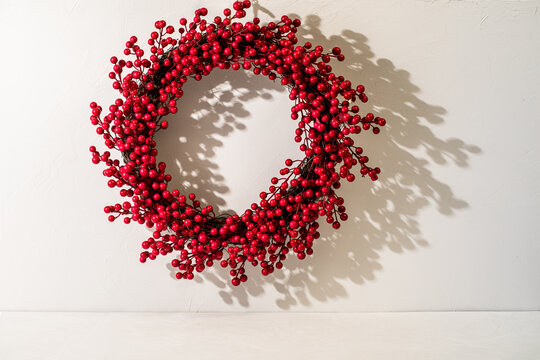 Red berry holiday wreath on white plaster 
wall