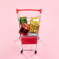 Fototapeta na wymiar Annual sale, Christmas shopping season concept - mini red shop cart trolley full of gift box isolated on pale pink background, copy space, close up