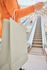close-up of a hand holding a paper bag of mockup on an escalator in a shopping mall