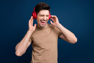 Portrait of ecstatic overjoyed man with stubble wear beige outfit touching headphones listen rock...